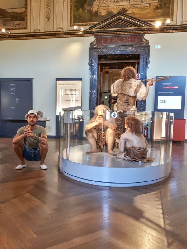 trener kucający w muzeum przy eksponatach pierwotnych ludzi